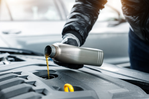  Een persoon vult motorolie bij in een Peugeot 208-motor, gebruikmakend van hoogwaardige synthetische olie zoals Fanfaro XTR 0W30.